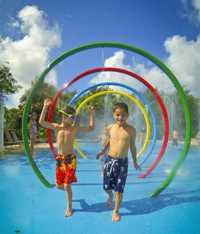 Two kids running through rainbow water loops on a splash pad